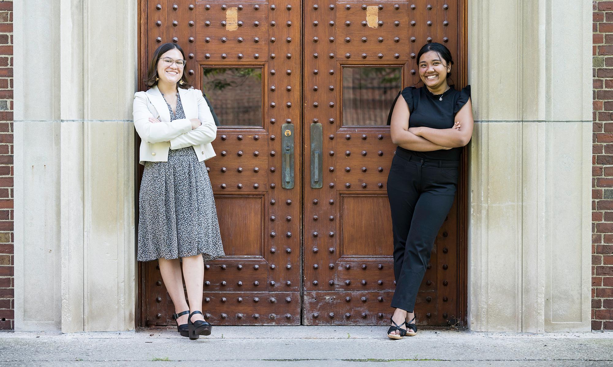 Mara Criollo-Rivera and Kristel Kezia Sagabaen Layugan smile as they pose for a photo leaning against the doors of Rush Rhees Library.